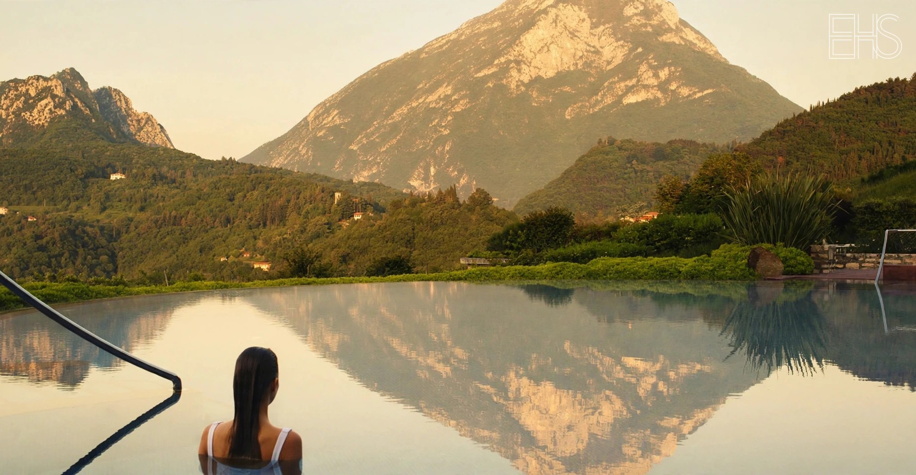 Lefay Resort's salt-water pool La Luna nel Lago at golden hour, mountains reflected in still water, a woman at the pool's edge