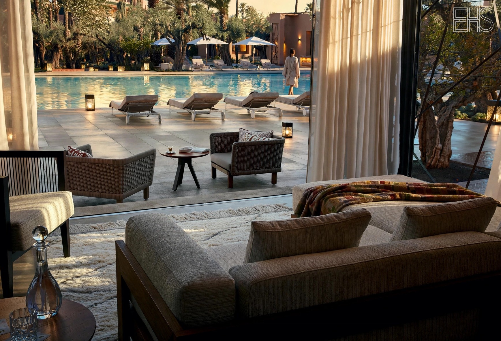 Woman in a linen robe walking beside the Le Jardin pool at Royal Mansour Marrakech at golden hour